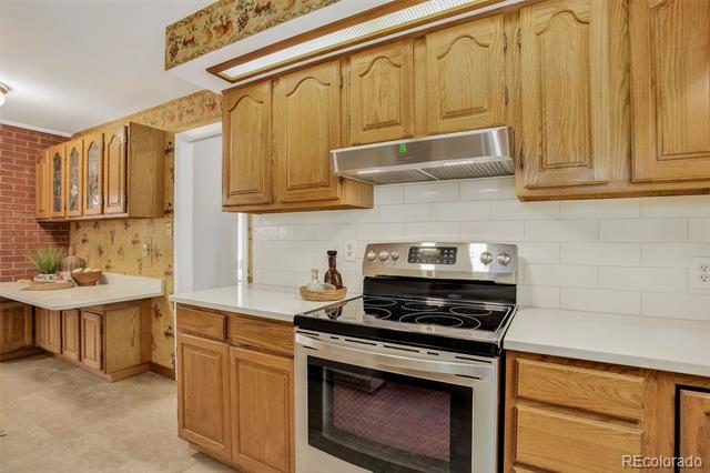 Kitchen with honey-colored wood cabinetry, white tile backsplash, and a stainless steel electric range.