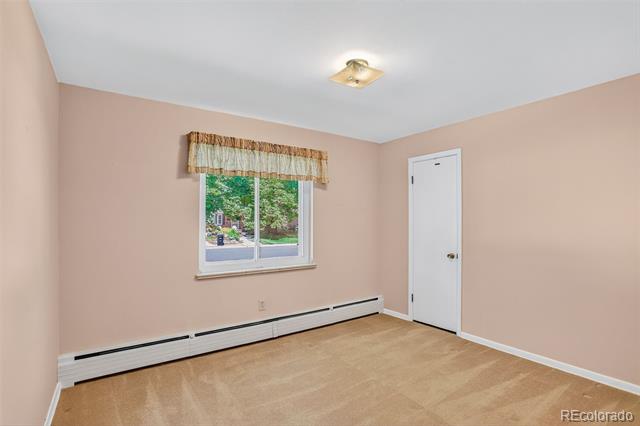 Empty room with light wood flooring, a window with a patterned valance, and baseboard heating.