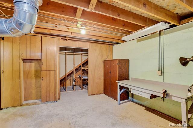 Unfinished basement workshop with exposed ceiling joists, ductwork, and a long workbench.