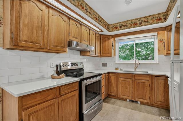 Kitchen with warm wood cabinets, white countertops, and a sink beneath a window overlooking trees.