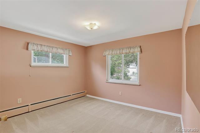 Empty bedroom with peach-pink walls, two curtained windows, beige carpet, and a long baseboard heater.