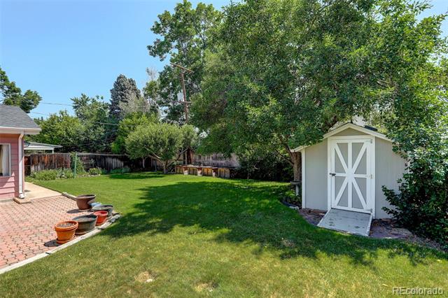 Backyard with a white garden shed, mature trees, green lawn, and brick patio.