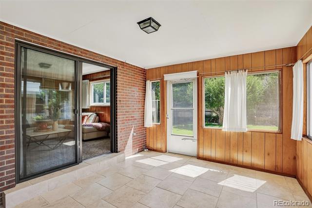 Enclosed patio with brick and wood-paneled walls, tile floor, and windows overlooking greenery.