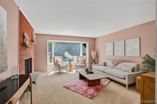 Staged living room with a brick fireplace, blush-pink walls, and a large window overlooking greenery.
