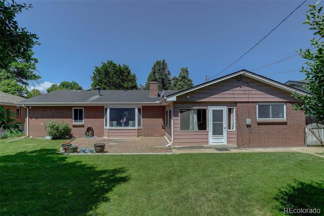 Rear exterior of a brick ranch home with a broad lawn and small patio.