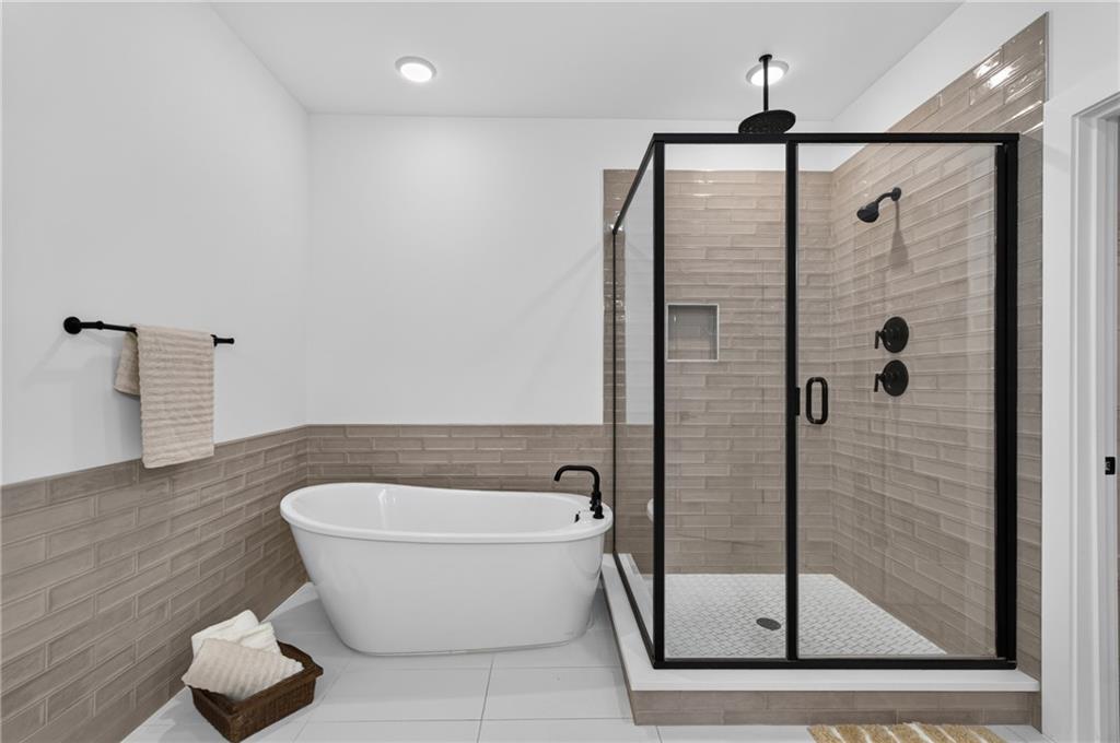 Bathroom with a freestanding tub beside a glass-enclosed shower with beige tile and black fixtures.