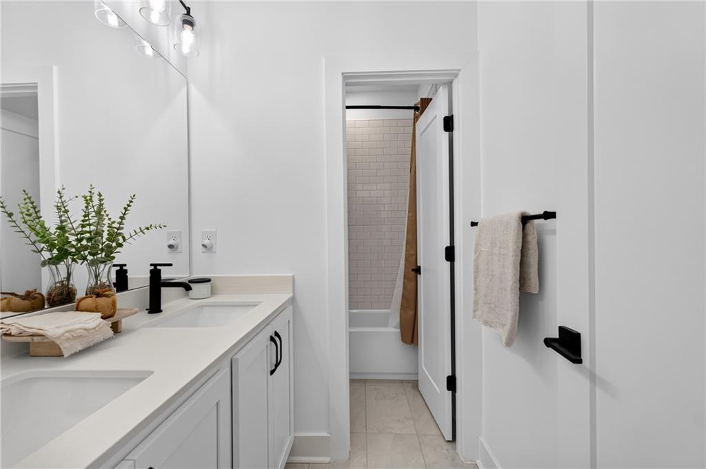 Bright bathroom with a white double vanity, black fixtures, and a tiled shower.