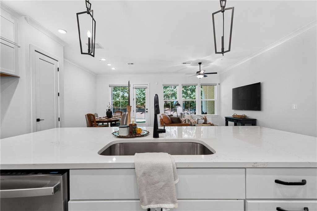 Kitchen island with a white countertop, stainless sink, and open living and dining area beyond.