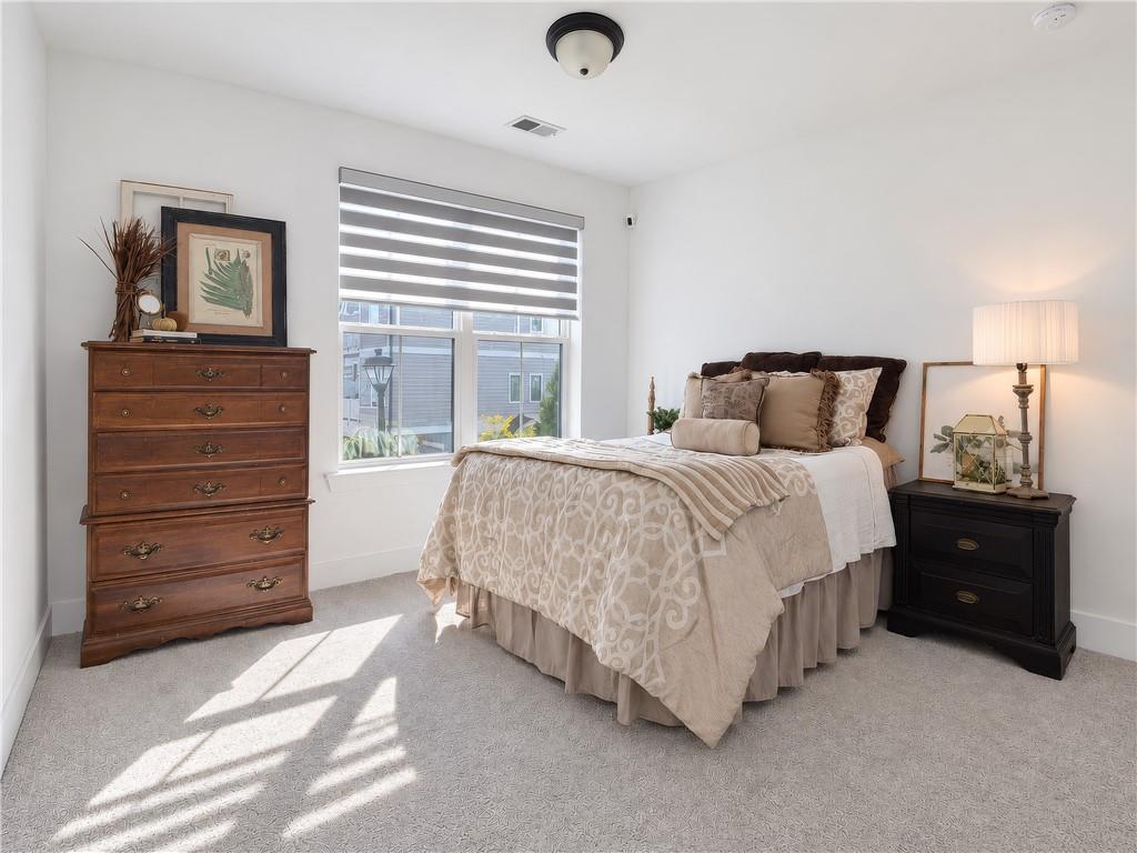 Staged bedroom with a large window, patterned bedding, and antique wooden dresser.