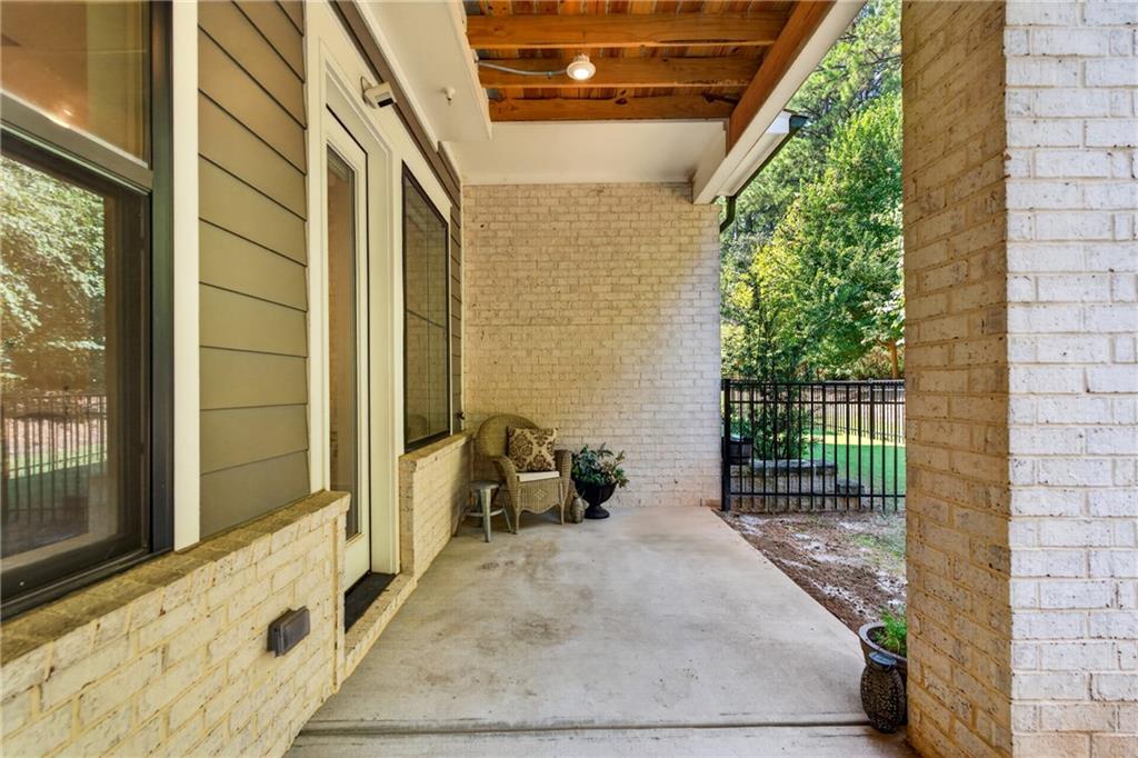 Covered patio with exposed wood ceiling, brick walls, and a small seating area overlooking the fenced yard.