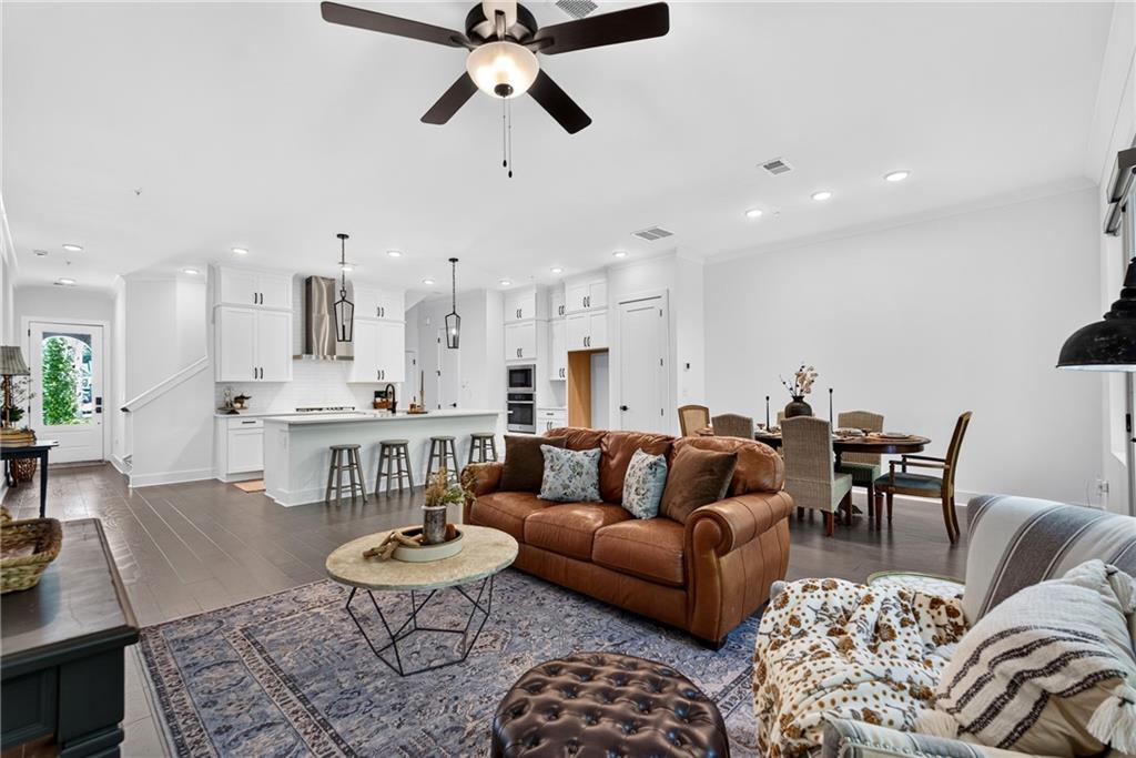 Open-plan living room and kitchen with a brown leather sofa, white cabinetry, and dining area.