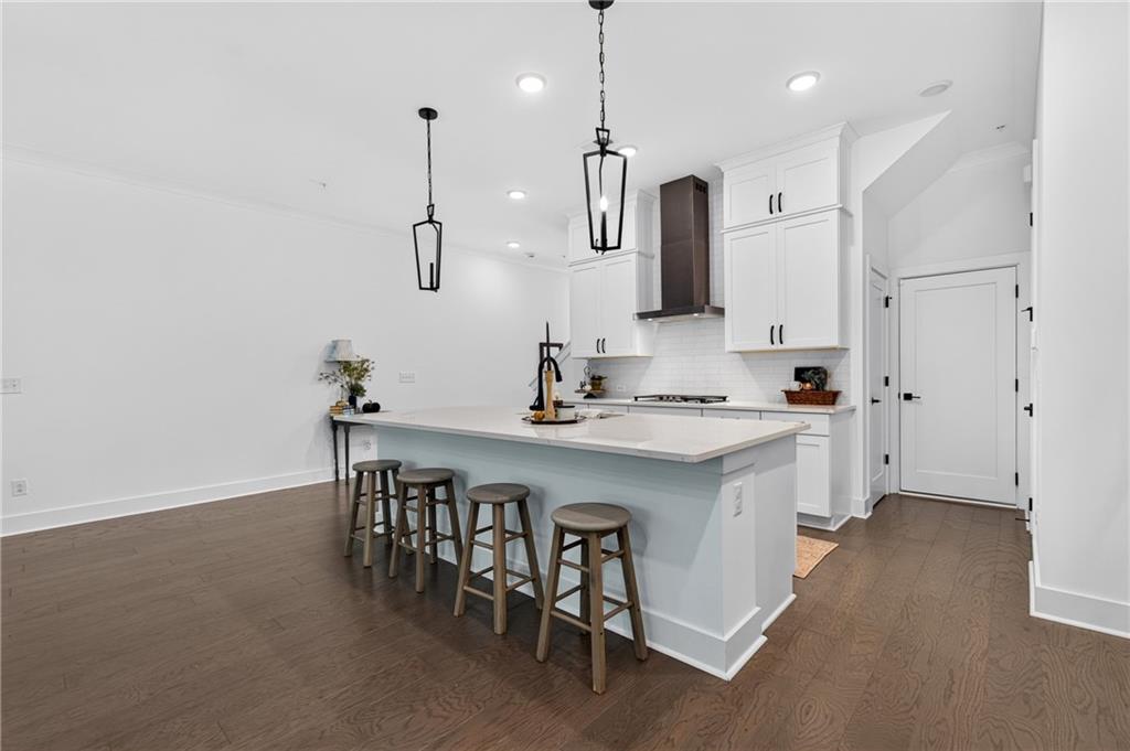 Kitchen with a large island, four stools, white cabinetry, and dark wood flooring.