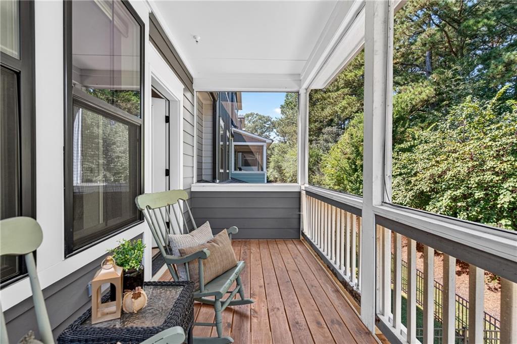 Covered porch with rocking chairs, wood flooring, and views of surrounding trees.