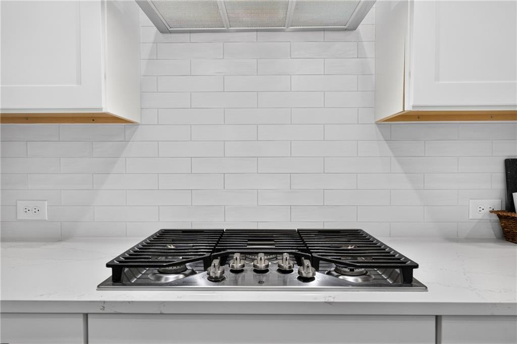 Kitchen cooktop set into a white countertop beneath a white tile backsplash.