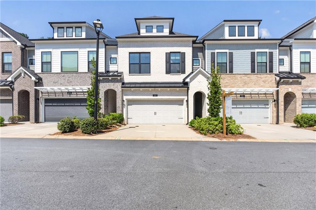 Townhouse with a light brick facade, white garage, and landscaped entrance.