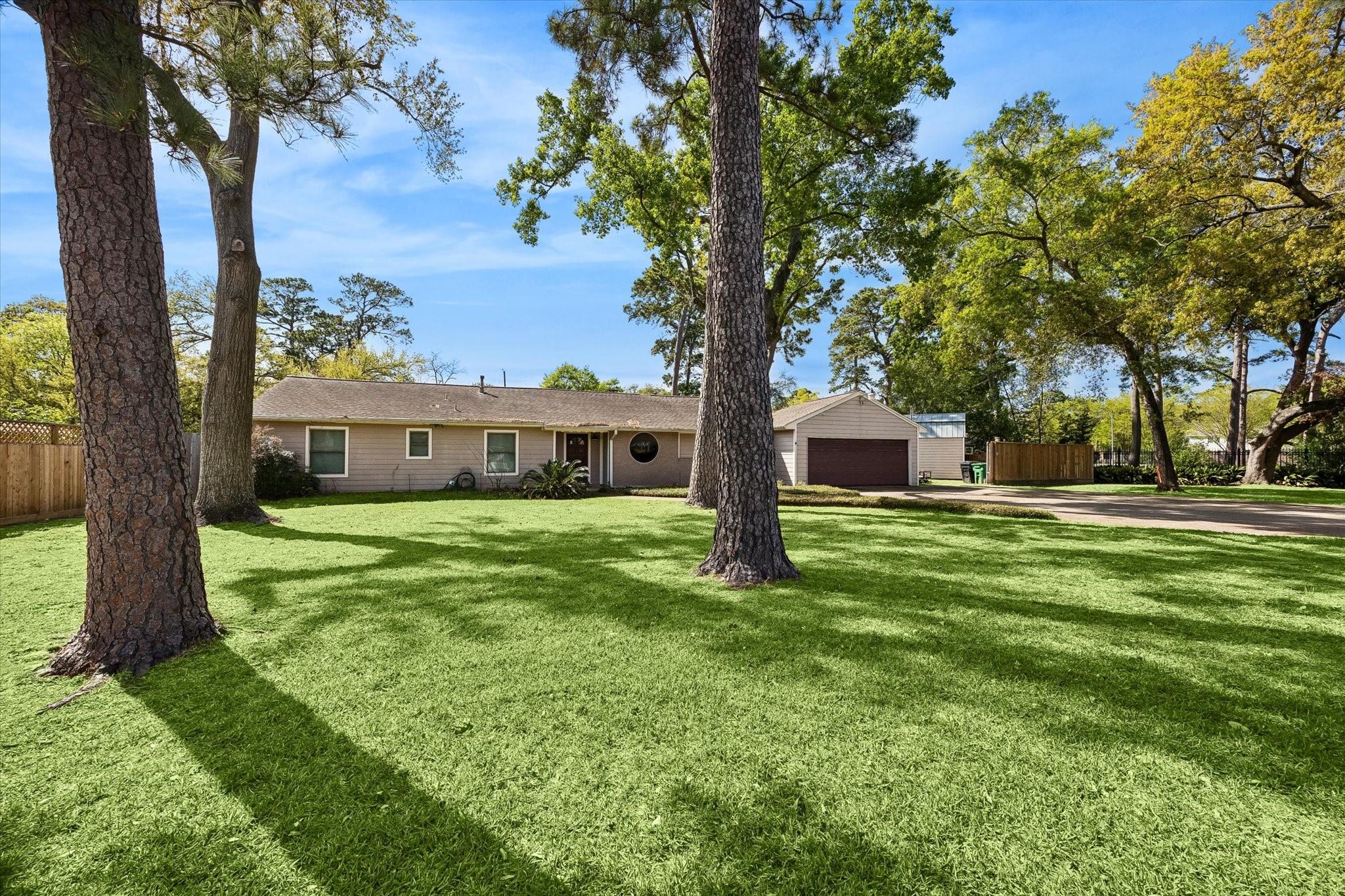 Single-story home with attached garage, circular front window, and a broad lawn shaded by mature trees.