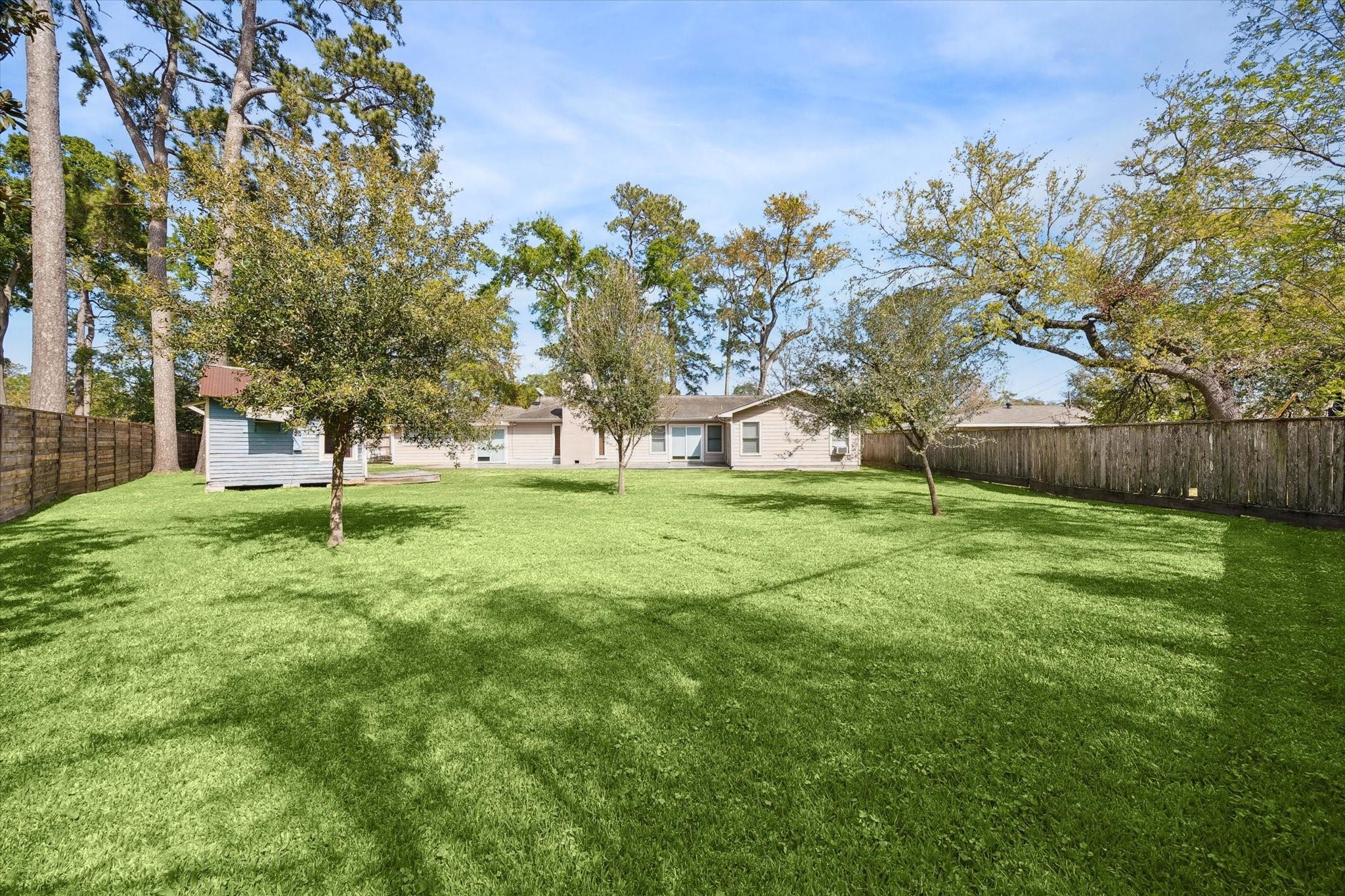 Spacious fenced backyard with a broad green lawn, mature trees, and a small shed.
