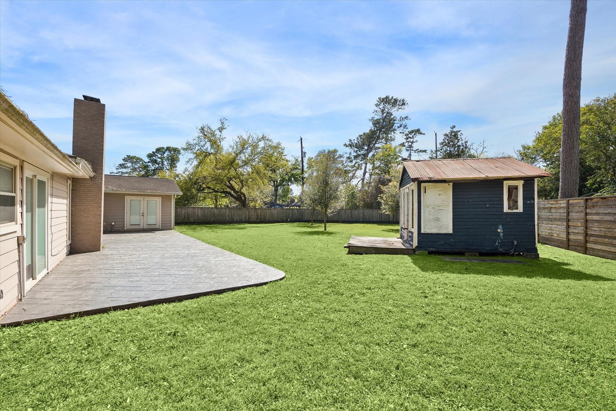 Backyard with a wide lawn, paved patio, and small dark shed beside the house.