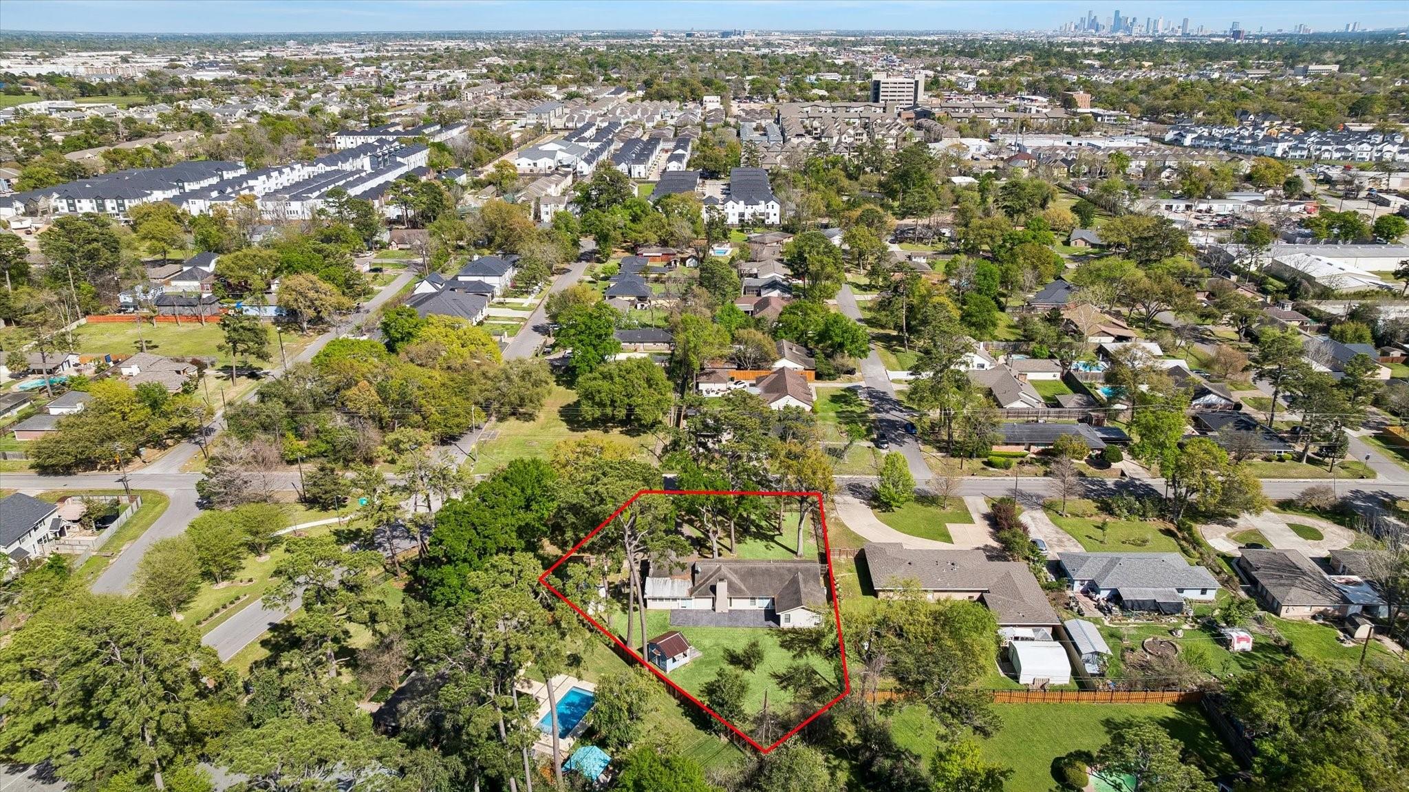 Aerial view of a tree-shaded home and outlined lot, with Houston skyline in the distance.