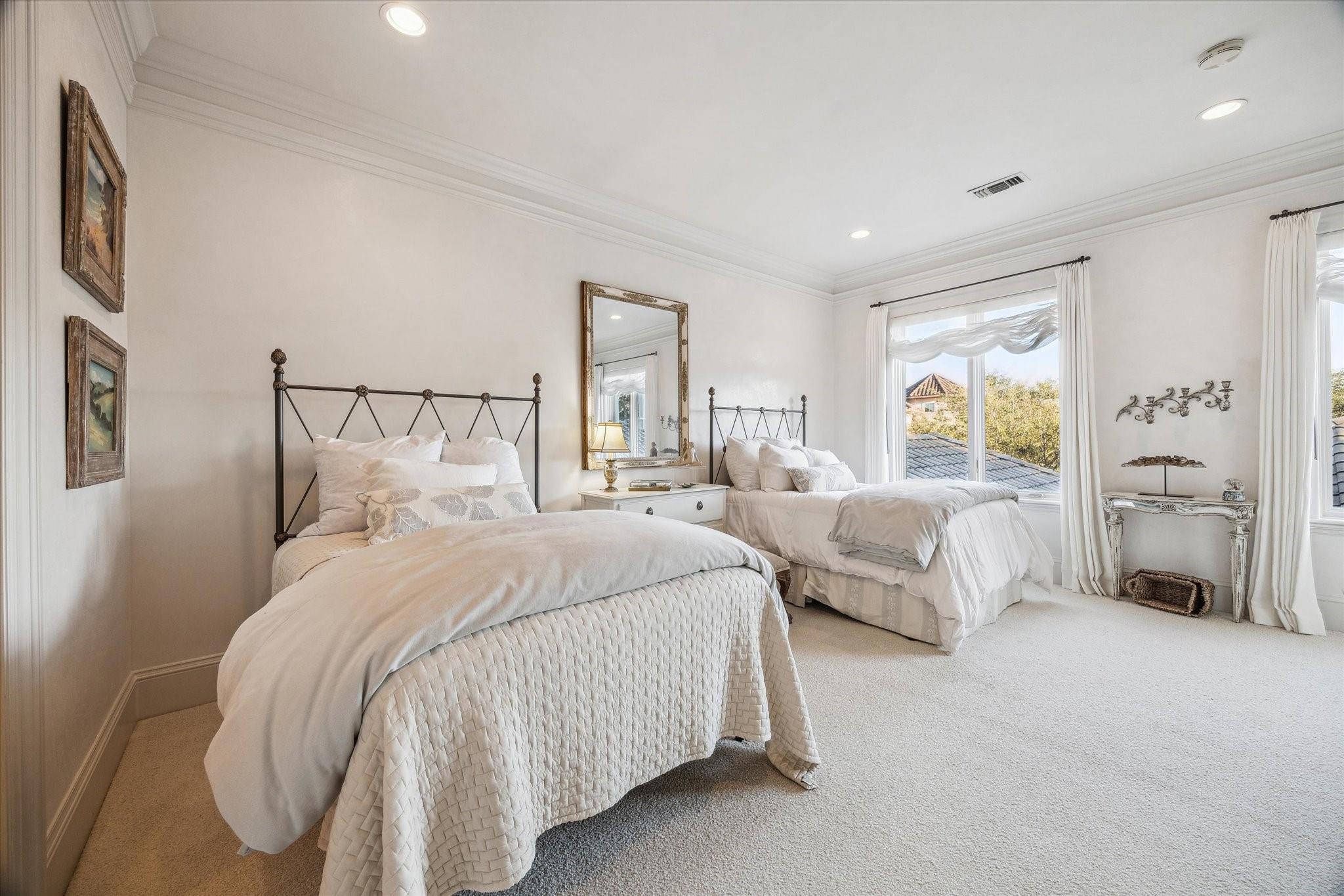 Bedroom with two white beds, dark metal headboards, and large curtained windows.