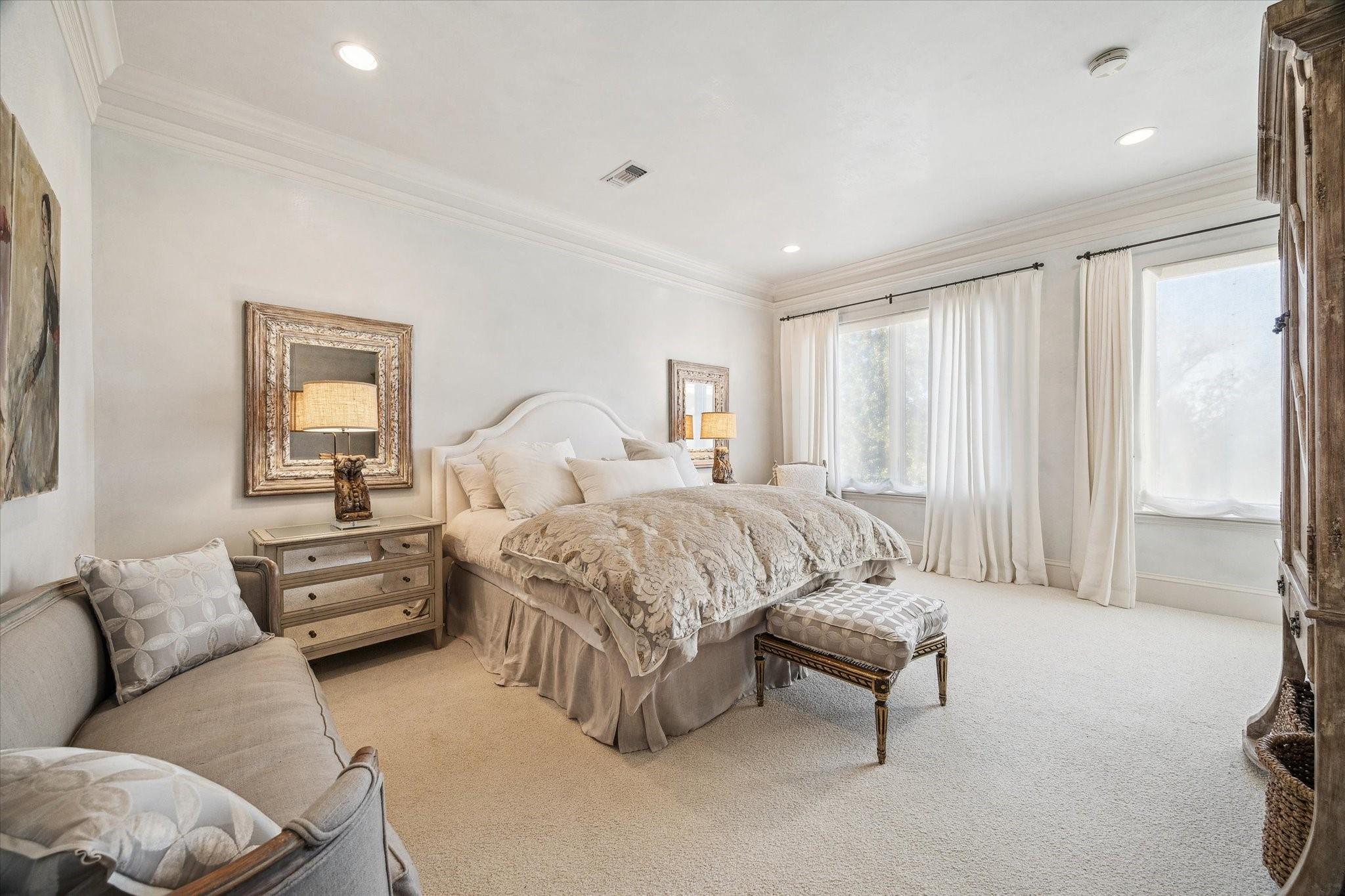 Furnished bedroom with a large upholstered bed, patterned bedding, and tall curtained windows.