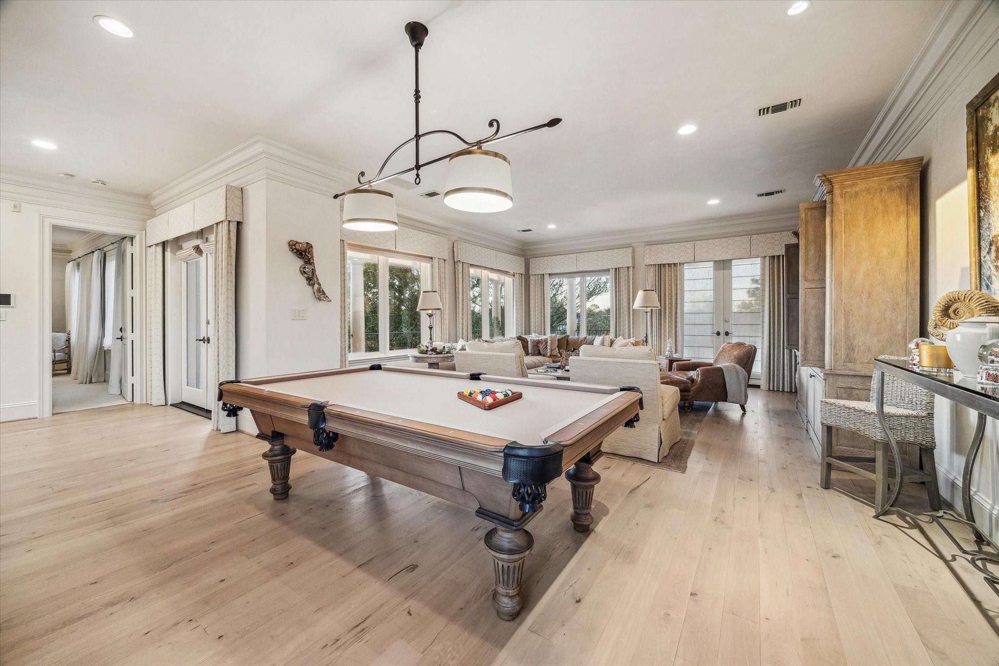 Game room with a large pool table, cream seating, tall windows, and wood cabinetry.