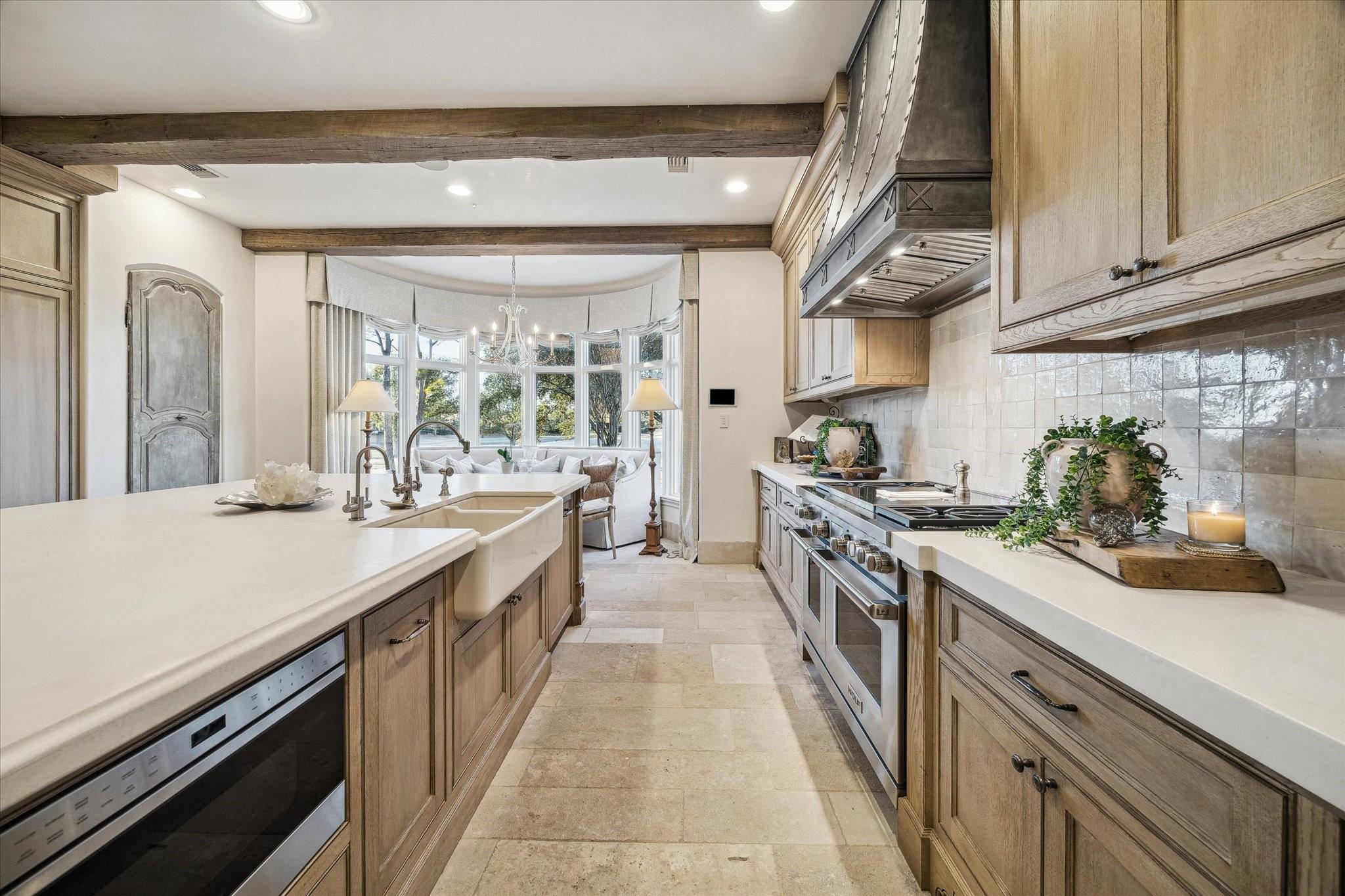 Kitchen with a farmhouse sink, warm wood cabinetry, exposed beams, and a bay window seating area.