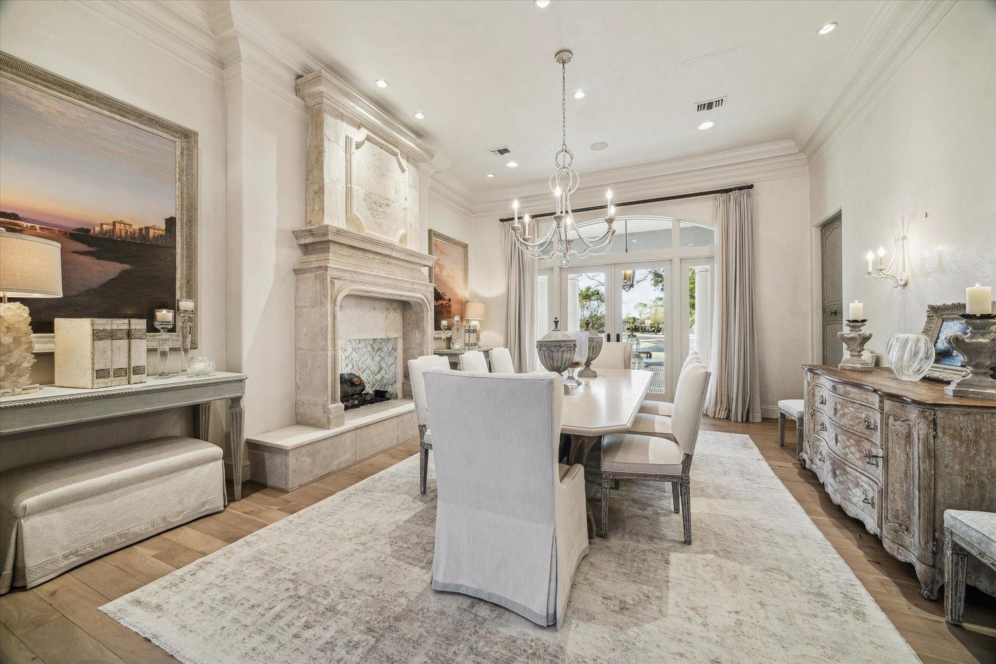 Elegant dining room with stone fireplace, chandelier, long table, and glass doors opening to patio.