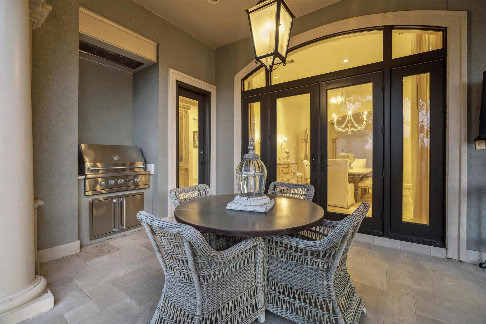 Covered patio with wicker dining set, built-in grill, and black-framed glass doors.