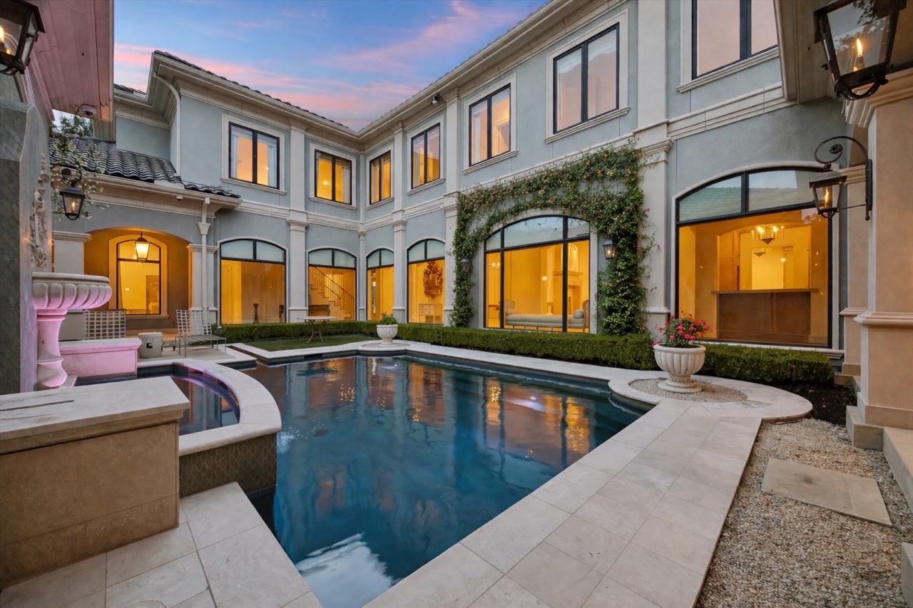 Two-story home surrounding a courtyard pool and raised spa at dusk.
