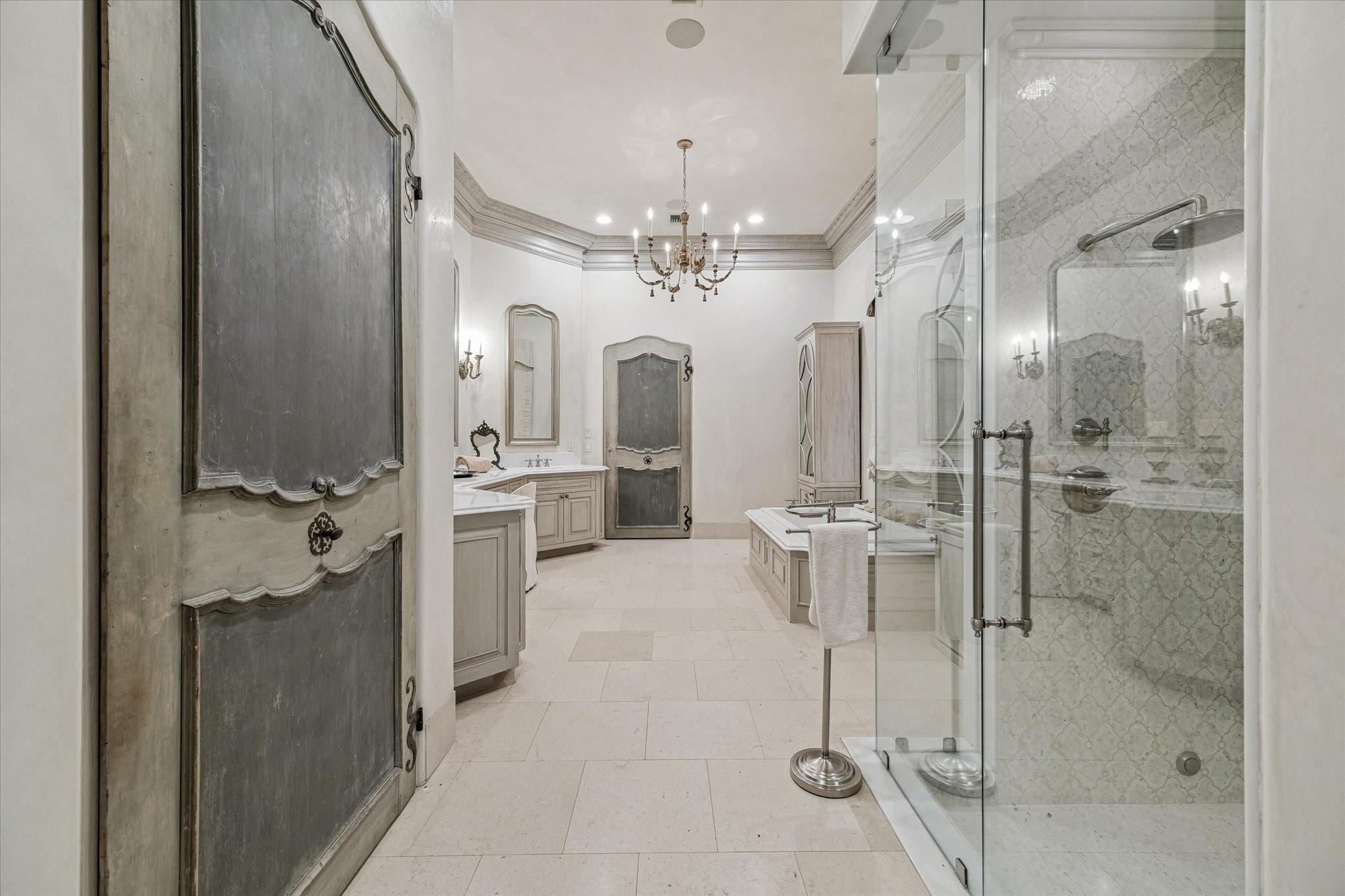 Spacious bathroom with a glass shower, patterned tile, double vanities, and an ornate chandelier.