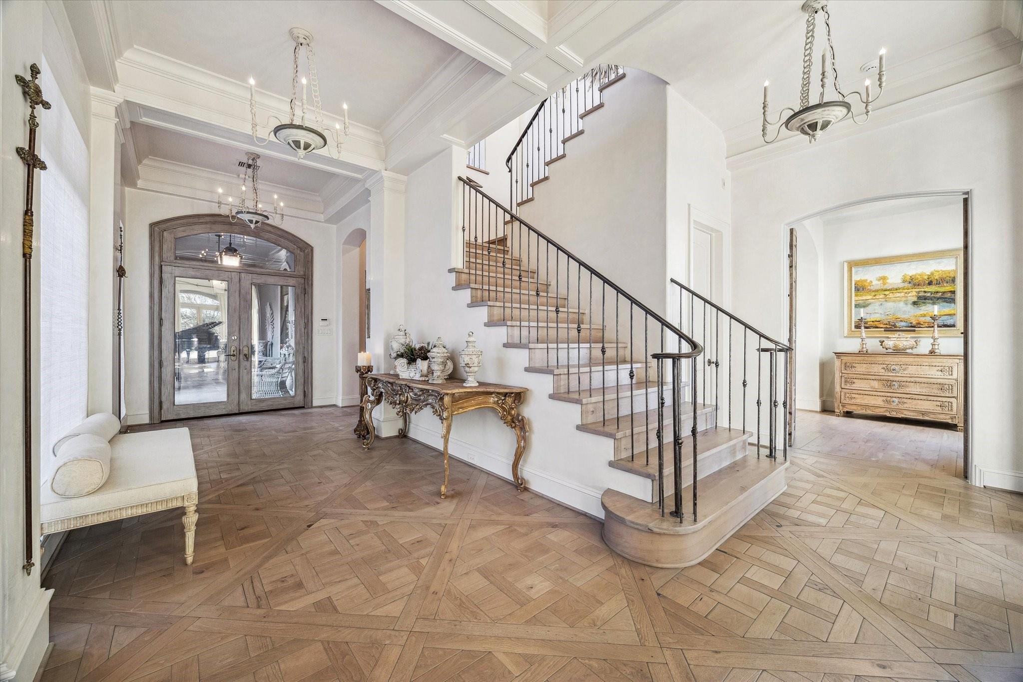 Foyer with a sweeping staircase, dark metal railings, and patterned wood floors.