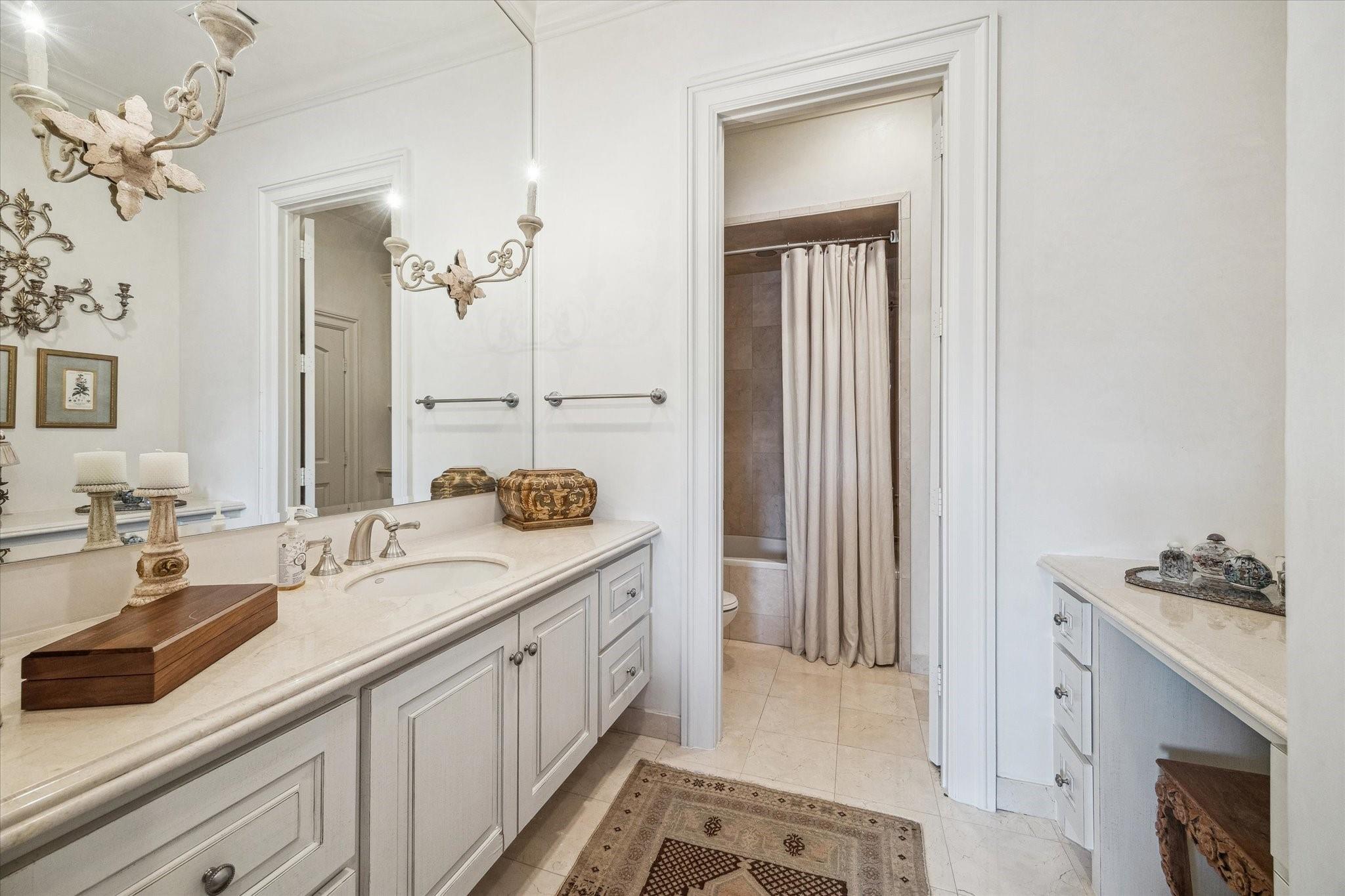 Bathroom with a long double vanity, pale stone counters, ornate chandelier, and curtained bathtub.
