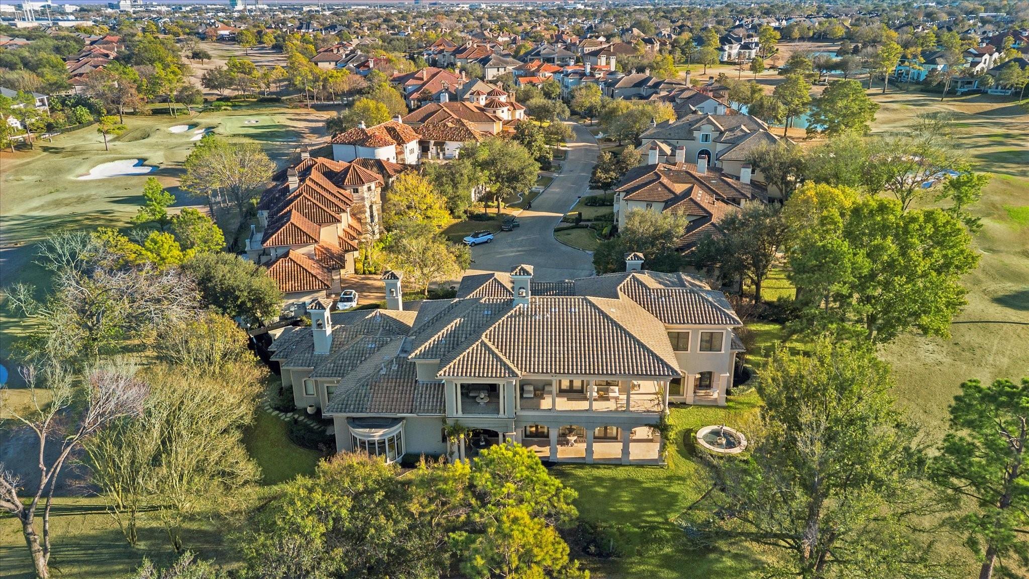 Aerial view of a large tiled-roof home with a covered patio, backyard fountain, and golf course nearby.