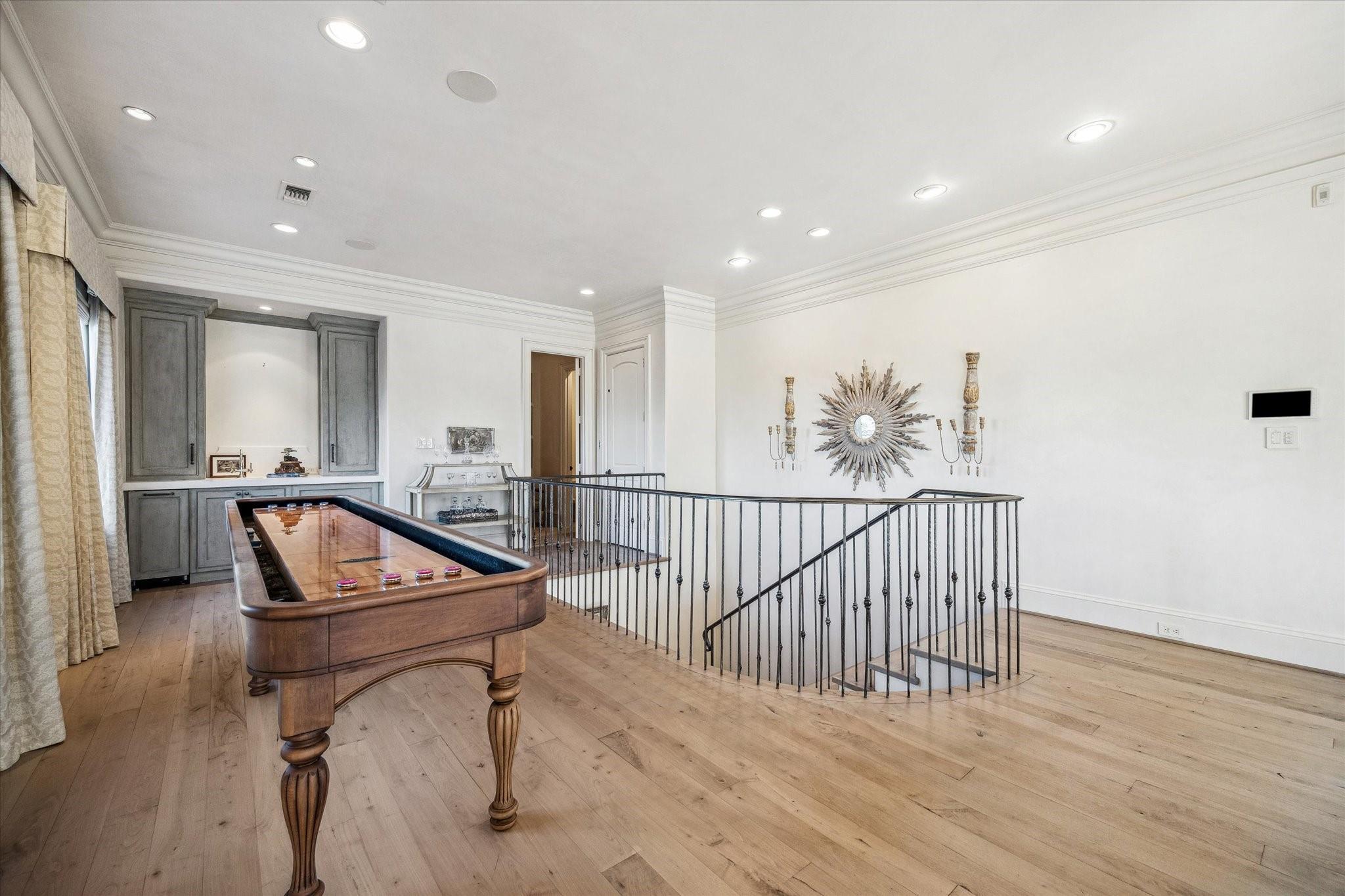 Upstairs game room with a wooden pool table and metal stair railing.