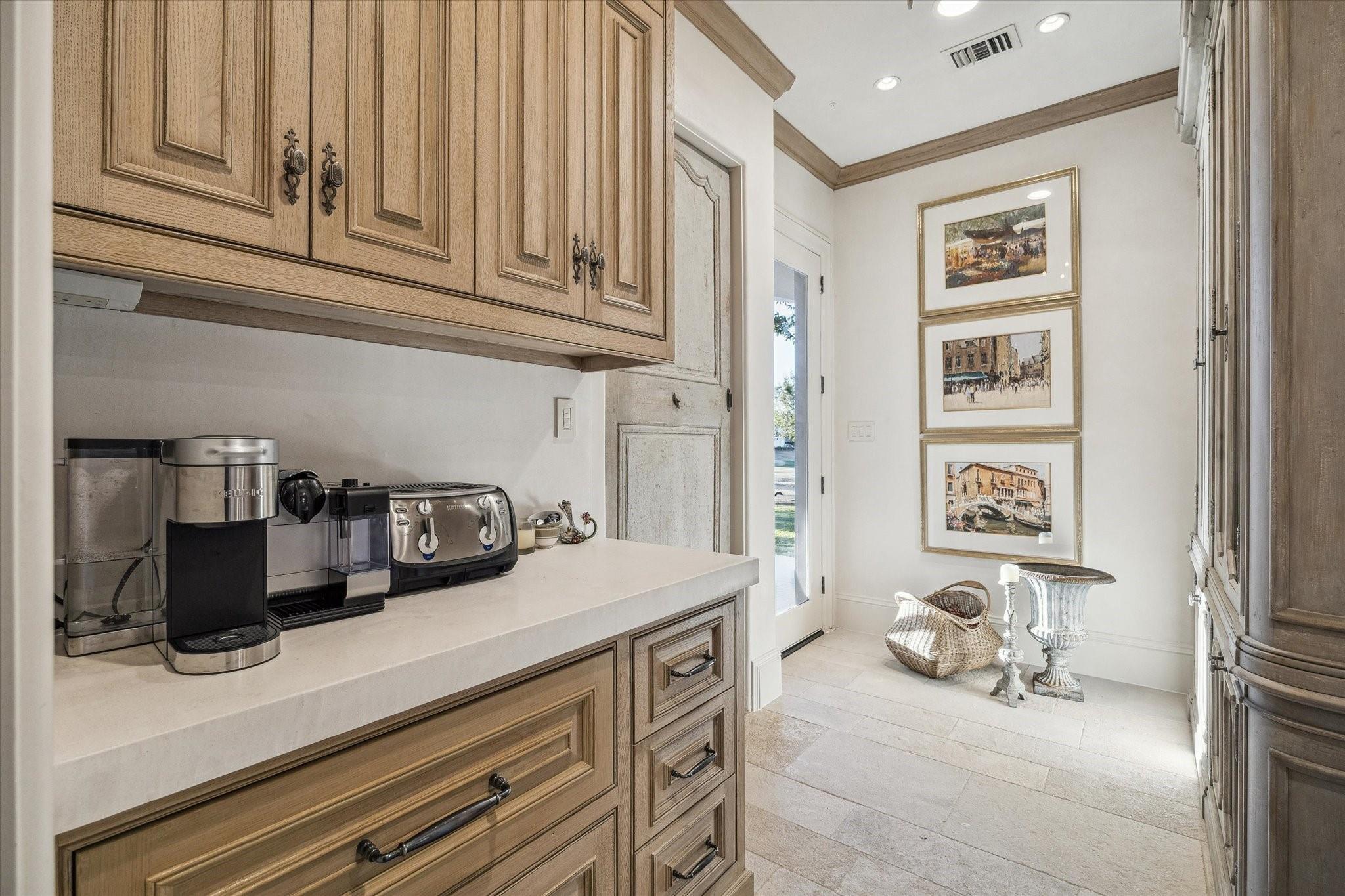 Kitchen with warm wood cabinets, coffee appliances, and a nook with framed prints and a wicker basket.