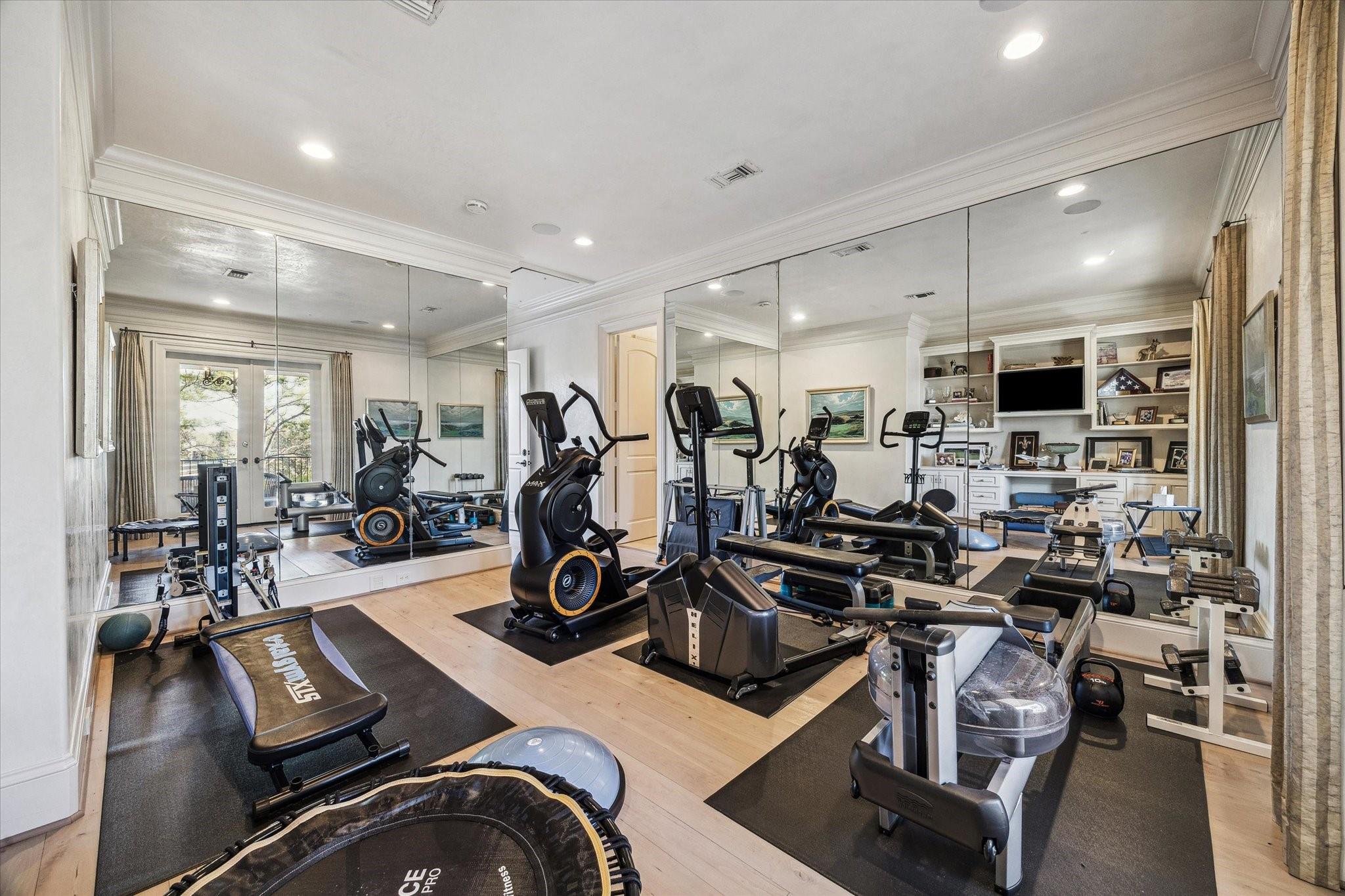 Home gym with mirrored walls, cardio machines, weight benches, and built-in shelving.