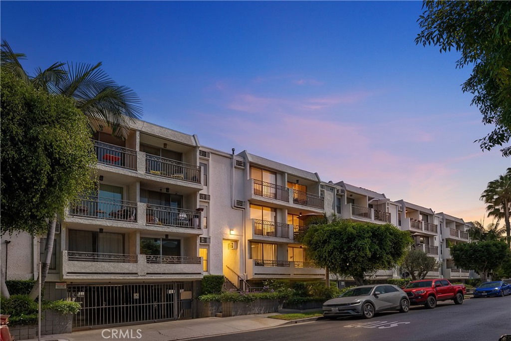 Multi-story condominium building with balconies and parked cars at dusk.