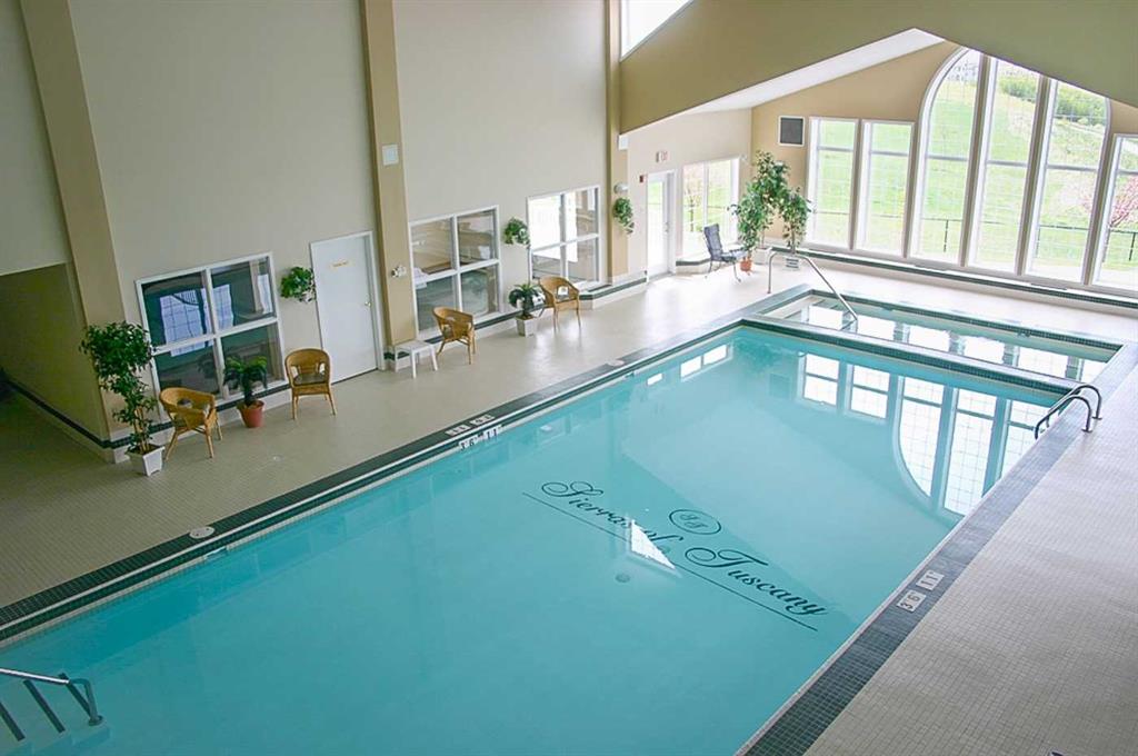 Indoor swimming pool with turquoise water, tall arched windows, and seating along the deck.