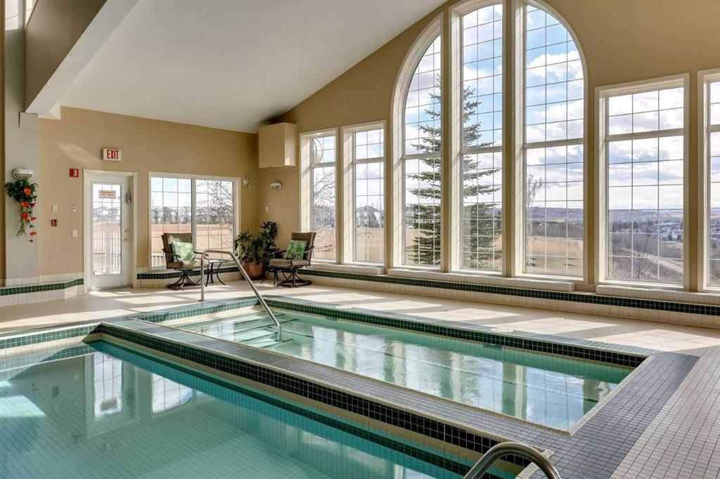 Indoor pool with a raised shallow section, stainless-steel handrails, and tall arched windows.