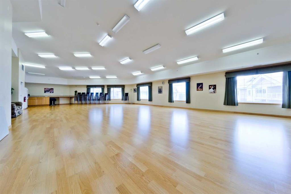 Community room with a wide polished wood floor, large windows, and chairs along the far wall.