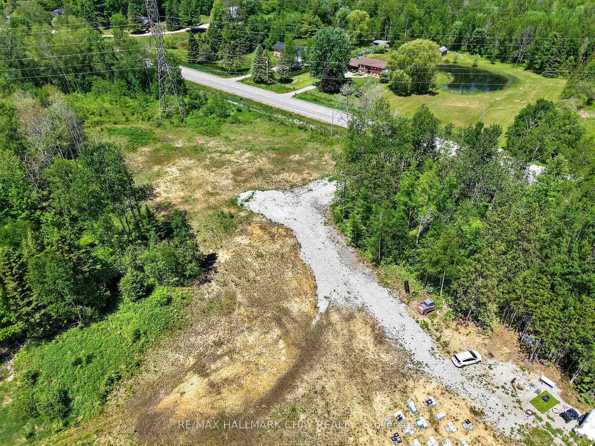 Aerial view of a cleared rural lot with a long gravel driveway and mature trees.