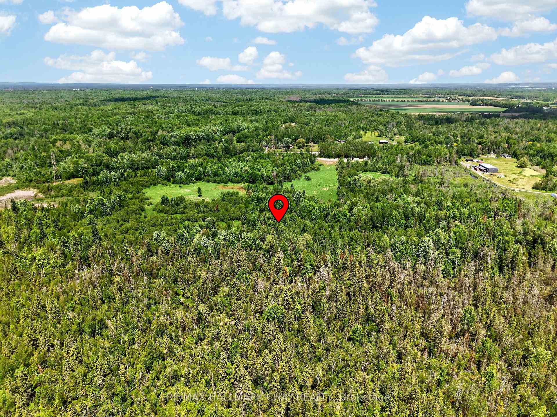 Aerial view of wooded rural land marked by a red location pin, with clearings and nearby fields.
