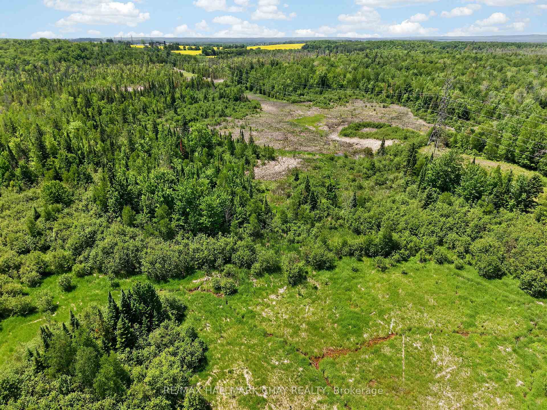 Aerial view of rural land with grassy clearings, dense woodland, and power lines.