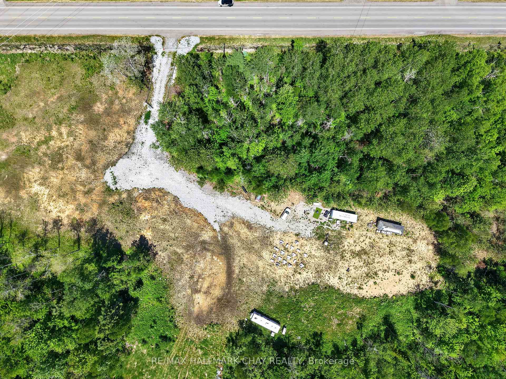 Aerial view of wooded property with a gravel driveway, open clearing, and access to the roadside.