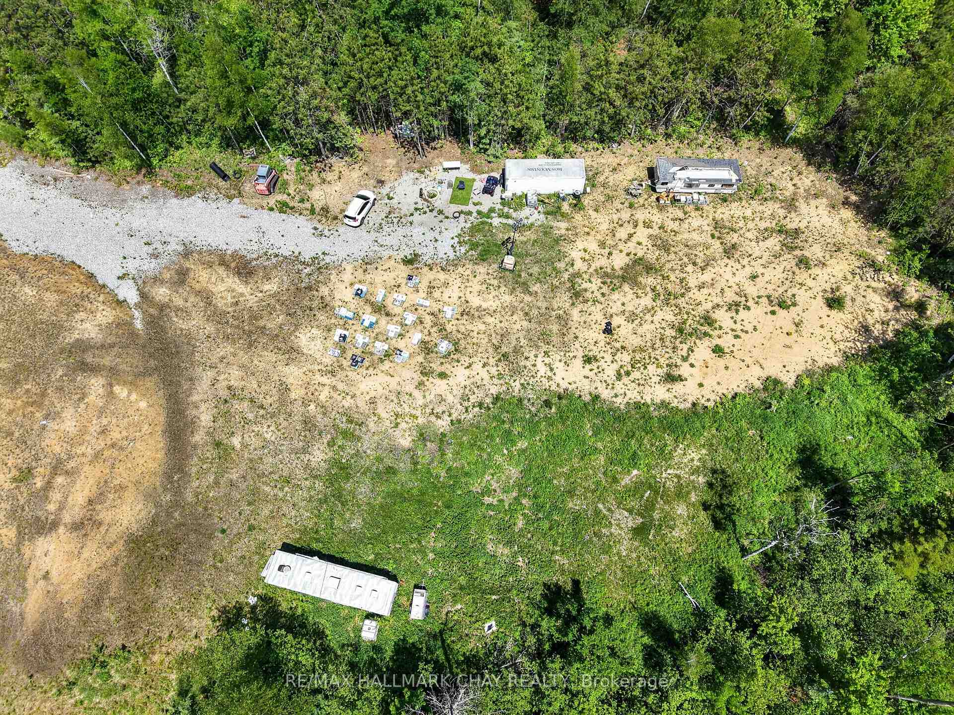 Aerial view of a partly cleared wooded property with a gravel drive and several trailers.