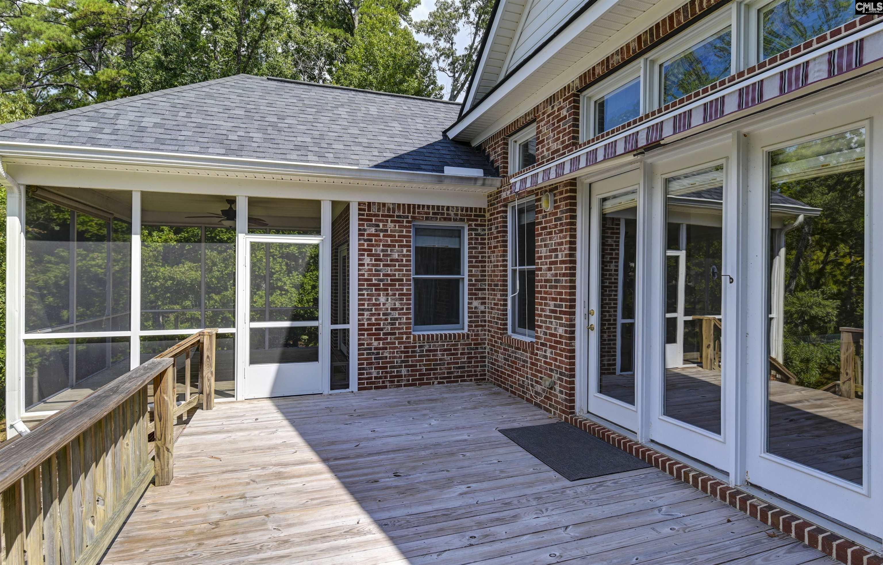 Wooden deck beside a brick house, with white French doors and an adjoining screened porch.
