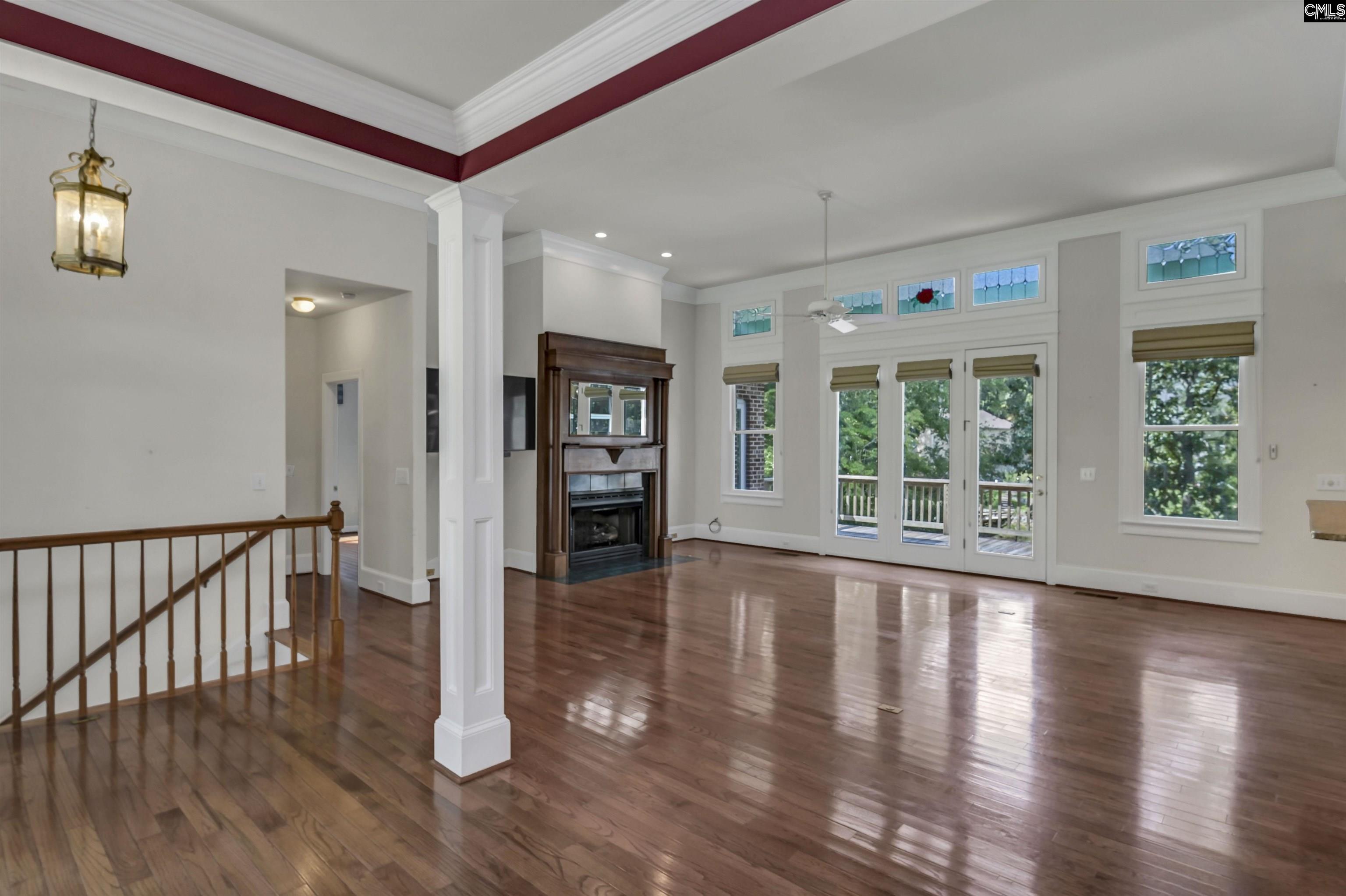 Empty living room with hardwood floors, a fireplace, and tall windows opening to a deck.