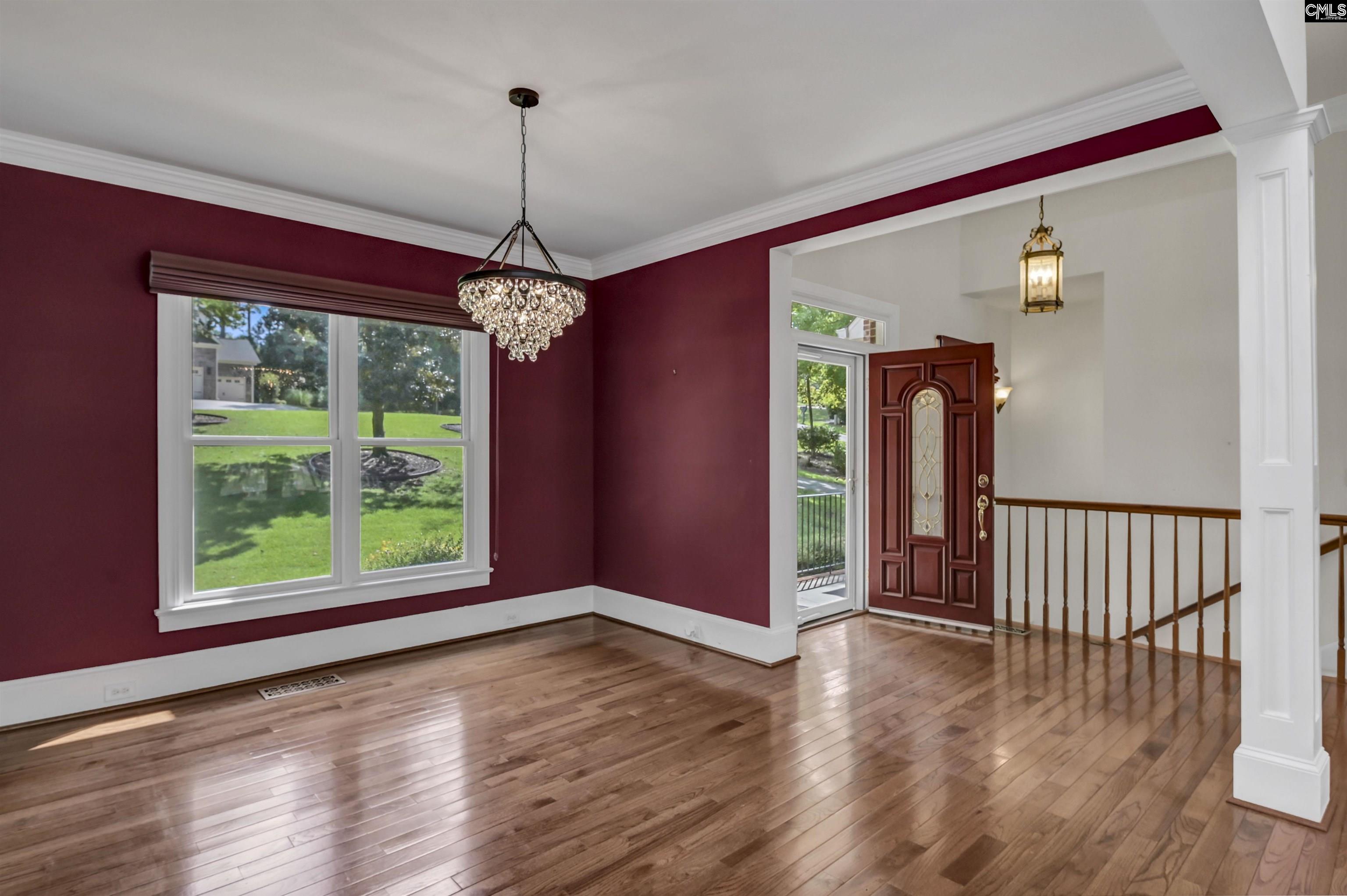 Entry area with burgundy walls, hardwood floors, a crystal chandelier, and an open front door.