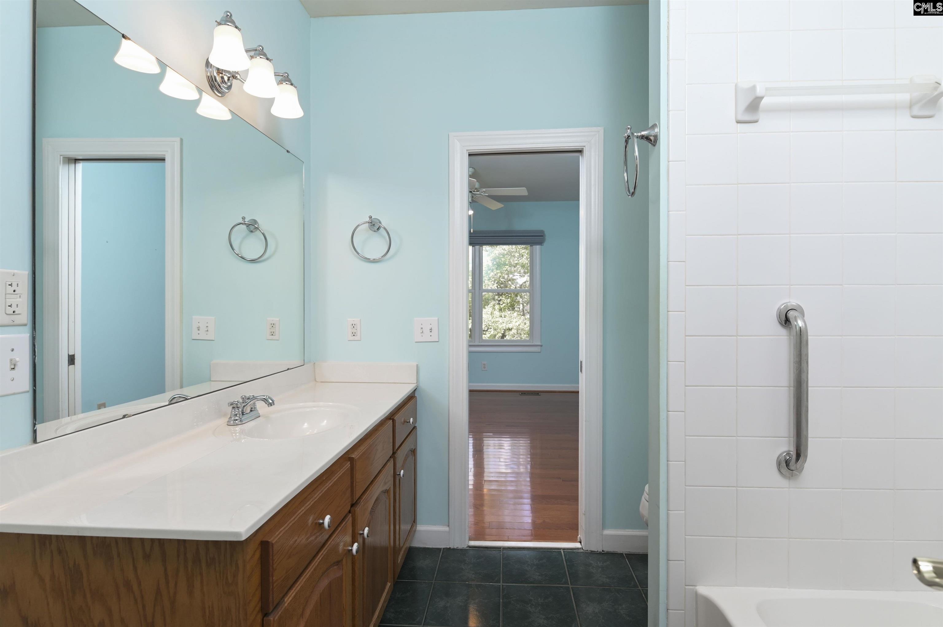 Bathroom with turquoise walls, a long white vanity, wood cabinets, and a tiled bathtub with grab bar.